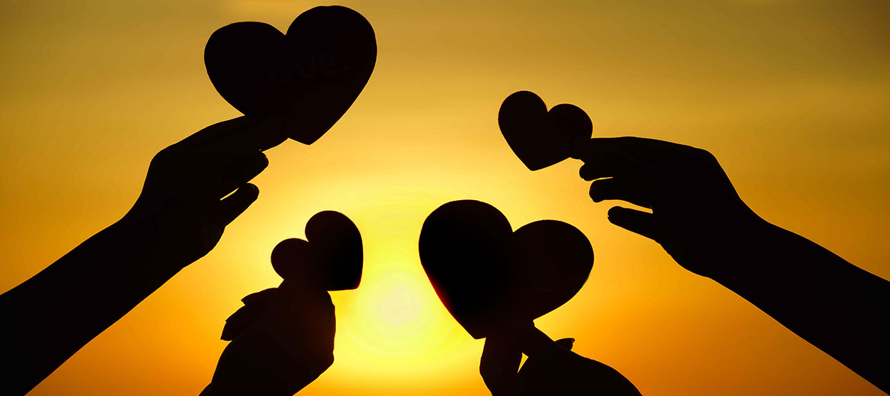 Image allégorique montrant quatre silhouettes de cœurs découpés dans du carton portés par quatre mains, l’ensemble de la scène est photographiée en contre-jour sur un coucher de soleil.