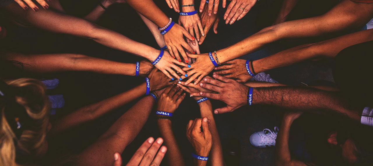 Groupe de mains croisées pour former une sorte d’étoile. Un bracelet bleu est visible sur tous les poignets.