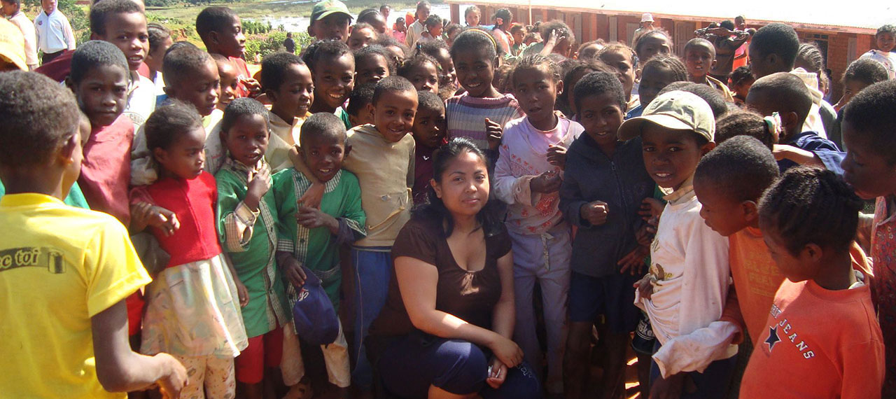 Groupe d’enfants dans un village à Madagascar. Ils entourent une jeune femme accroupie au milieu du cercle que forment les enfants.