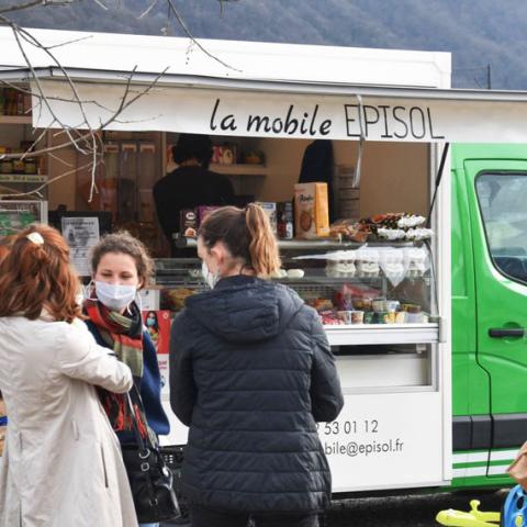 Camionnette vert et blanc de l’épicerie mobile EPISOL. Trois clientes discutent devant la camionnette, une autre cliente est en train d’être servie. Un client attend son tour. Ils portent tous des masques, la photo a été prise durant la Covid 19.