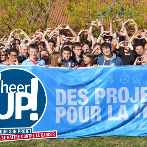 Portrait de groupe des équipes de l’association CHEER UP et des bénéficiaires. Ils soutiennent une banderole indiquant “Des projets pour la vie” devant eux. Ceux qui sont en arrière-plan font le signe du cœur. 